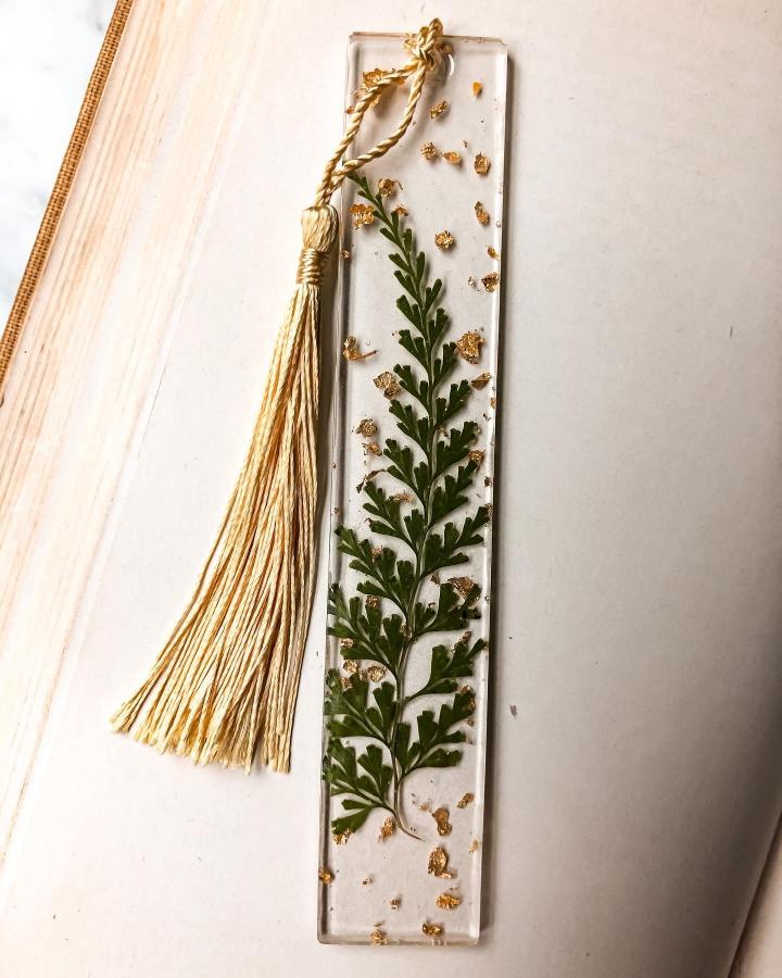 Green pressed fern bookmark with gold leaf bits and cream tassel from @nocturneworkshoppnw. Clear resin pressed leaf crafts detail.