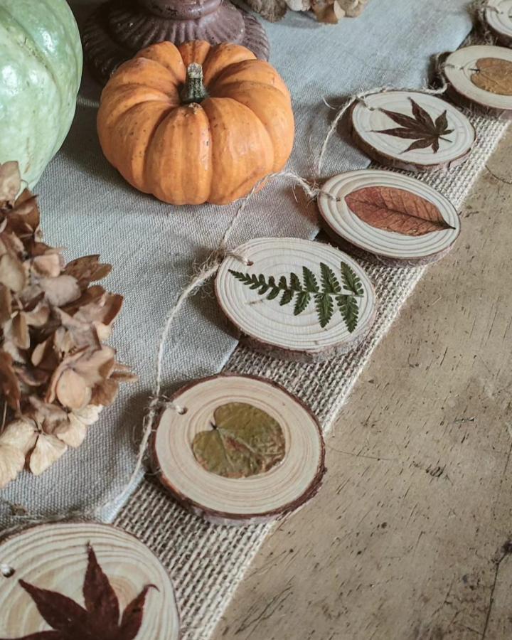 Orange pumpkin and natural wood slice garland with pressed leaves from @pulp_and_pigment. Rustic autumn pressed leaf crafts decor.