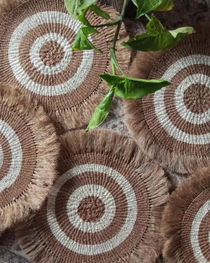 Brown and cream woven sisal jute placemats with fringe edges by @mila_zetu. Rustic natural fiber table decor with circular pattern.