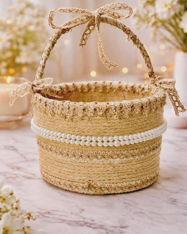 Natural jute rope basket decorated with white pearls and lace bows by @craftery_loom on marble surface. Rustic and elegant charm.