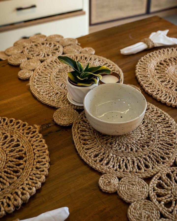 Natural jute woven placemats and table runner by @thekoshastore showing rustic handcrafted dining decor with plant and ceramic bowl.