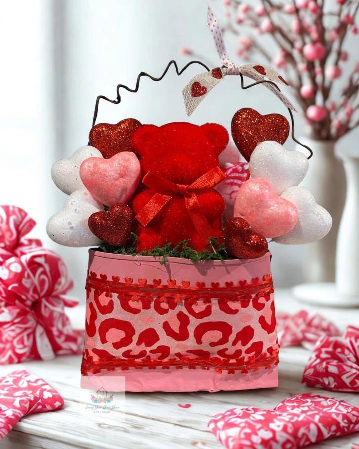 Pink and red decorated recycled container craft with heart and bear accents by @marylou_solorzano on a white wooden surface. Festive Valentine theme.