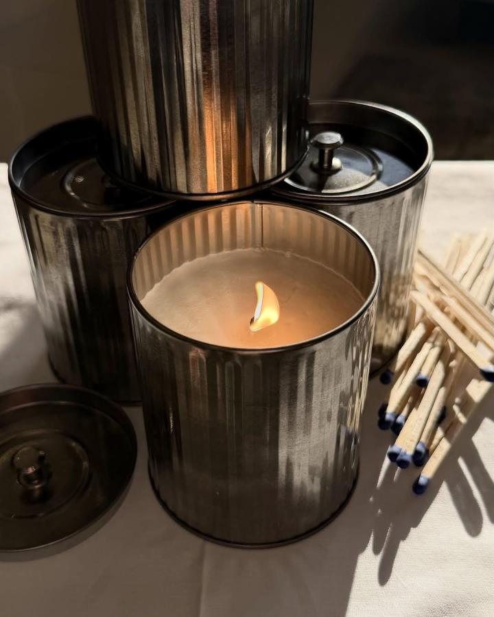 Silver ribbed metal candle holder made from recycled containers by @reemistudio. Rustic, cozy design with warm candlelight inside.