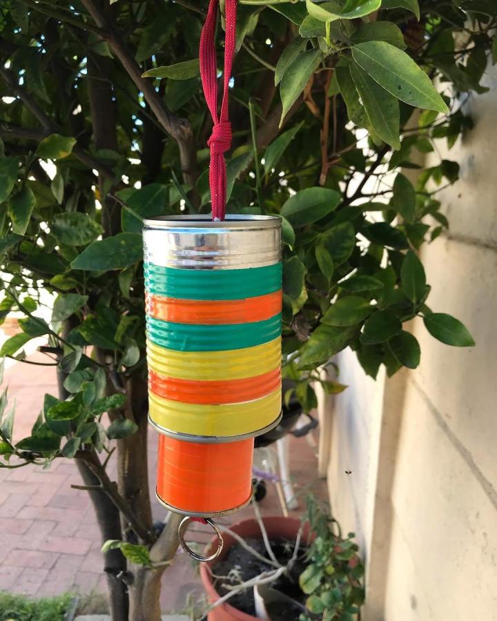 Brightly painted striped tin can wind chime hanging outdoors from @gramelley. Colorful recycled metal garden decoration.