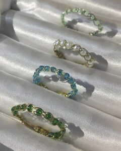 Green and blue beaded delicate wire rings from @carneliangarnet gleaming softly on satin fabric surface handcrafted stackable accessories.