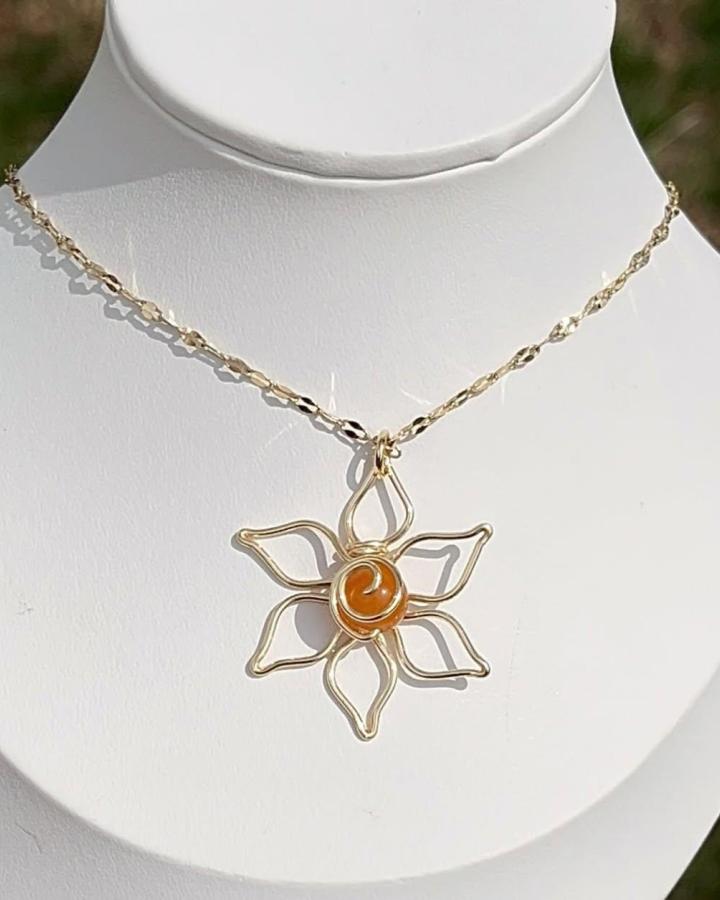 Gold wire flower pendant with amber bead center necklace from @getstonedbyamber. Elegant handmade jewelry with twisted petals and warm hues.