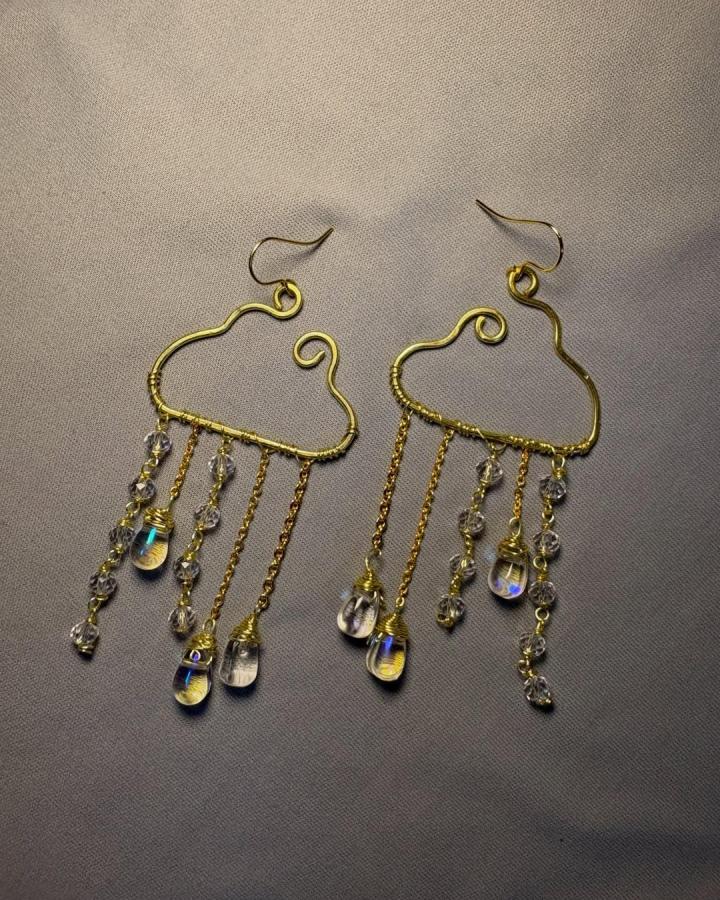 Golden cloud-shaped wire earrings with crystal bead raindrops hanging on delicate chains by @an.n.ash. Elegant and whimsical jewelry design.
