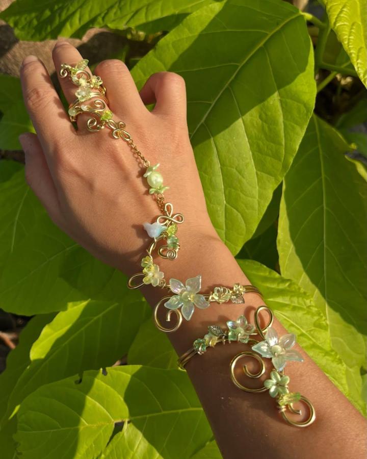 Delicate gold wire hand chain with soft green beads and flower details from @whenibroke.myleg, showing intricate jewelry craft.