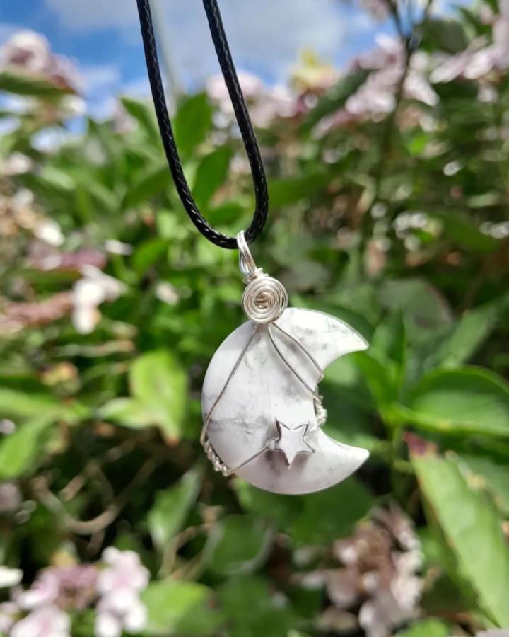 White marble crescent moon pendant with silver wire and star detail from @lui.na.greine hanging on black cord outdoors. Nature background.