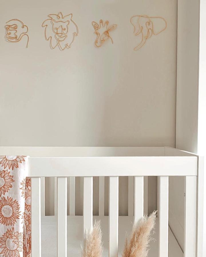 Gold wire nursery wall art from @rosewiredesigns featuring minimalist animal face silhouettes above white crib. Soft neutral nursery decor.