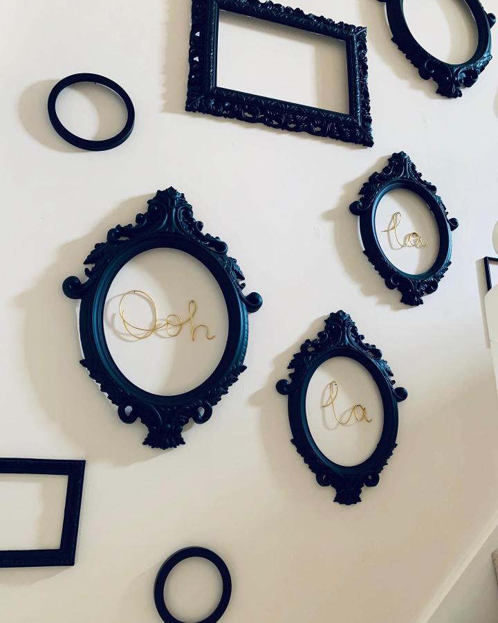 Black ornate frames on wall with gold wire script inside from @knackeredmavis. Contrast of vintage style and modern wire lettering.