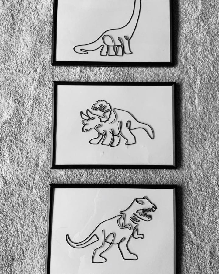 Black wire dinosaur sculptures framed on white backgrounds from @wiredandwonderfuldesigns. Minimalist kids room wall decor with playful charm.