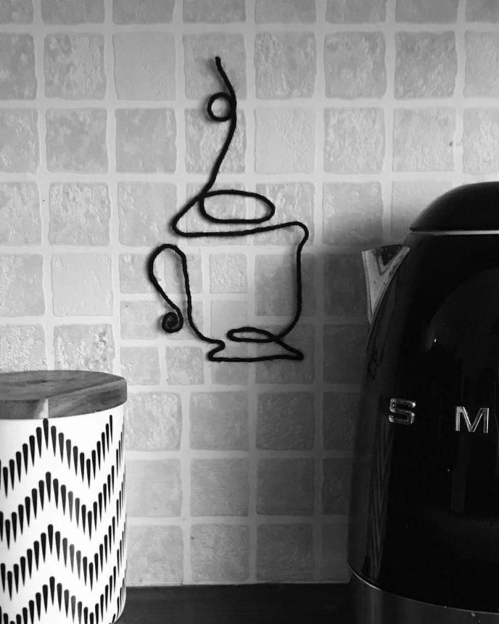 Black wire kitchen wall art by @jessfirth_art. Minimalist coffee cup shape with playful linework near countertop.