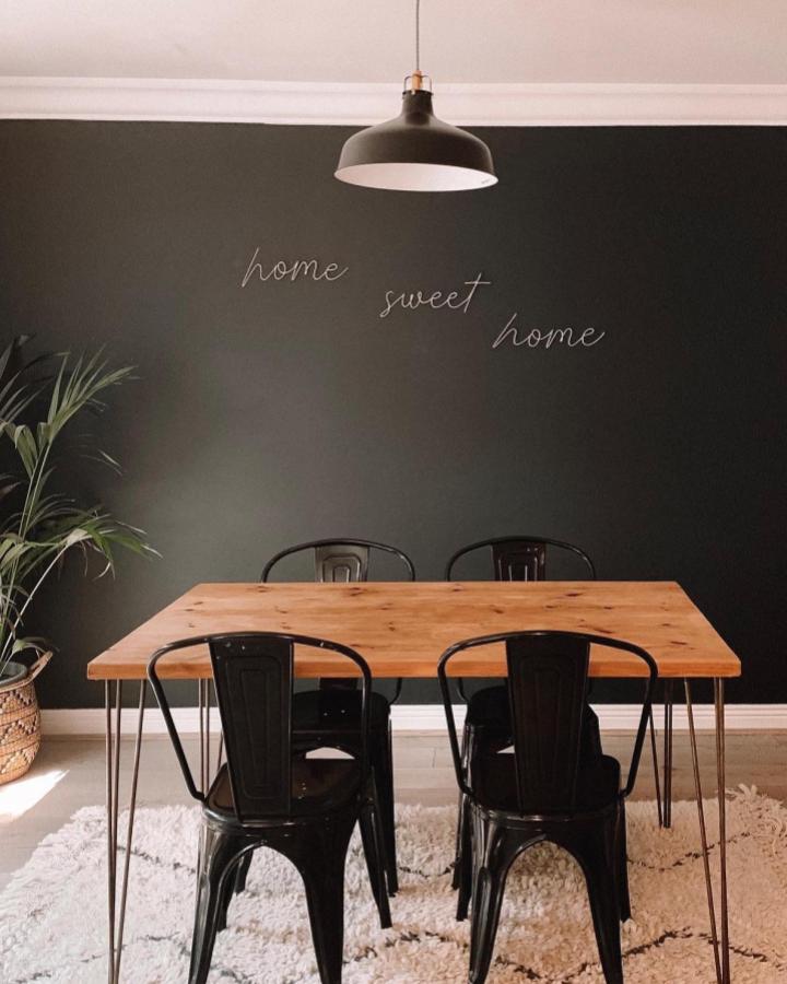 Black wire script letters on matte black wall in a minimalist dining room from @rosewood.home. Subtle, handwritten style art for cozy home vibes.