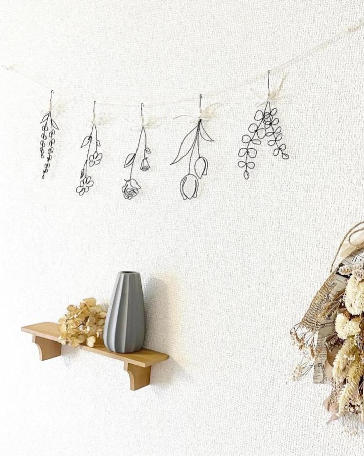 Black fine wire hanging floral garland from @nana.wire_art. Minimalist botanical wall decoration with delicate loops and curves.