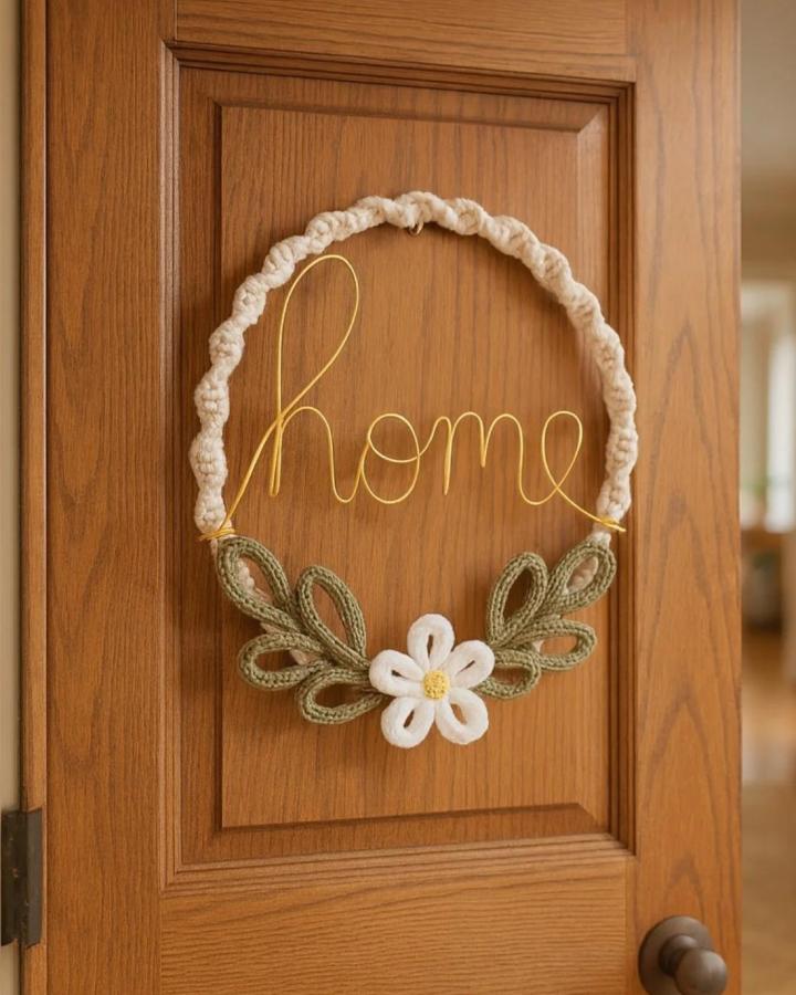 Golden wire word art wreath with olive green loops and a white flower crafted by @cozy_craft_canada. Cozy macramé style welcome sign.