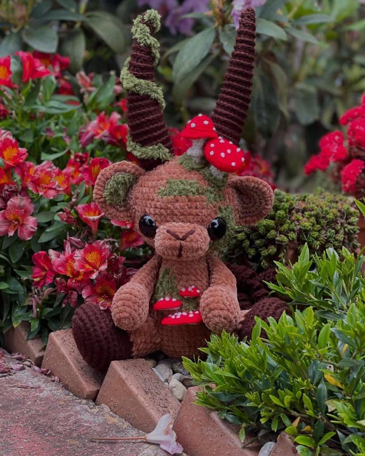 Brown and green plush crochet woodland creature with red mushrooms from @hookandcauldron perfect for woodland crochet pattern ideas. Cute nature-inspired amigurumi with textured horns.
