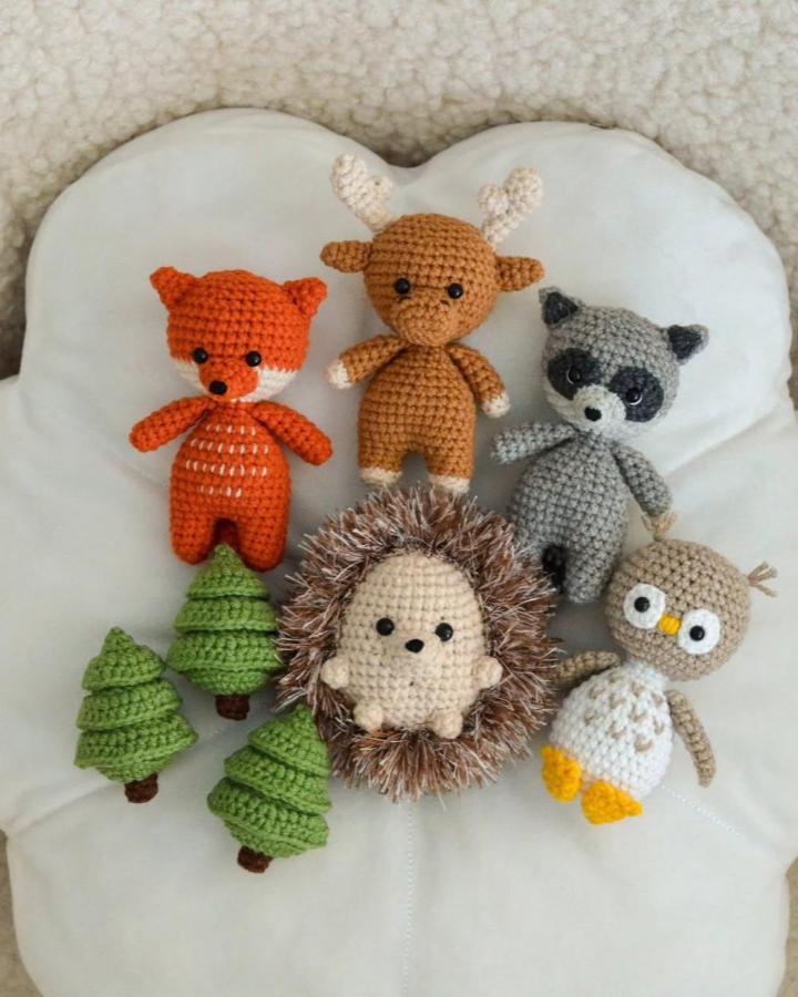 Orange fox, brown deer, gray raccoon, and textured hedgehog crochet toys with green trees by @pupsik_toys.ua. Cute forest animal crafts.