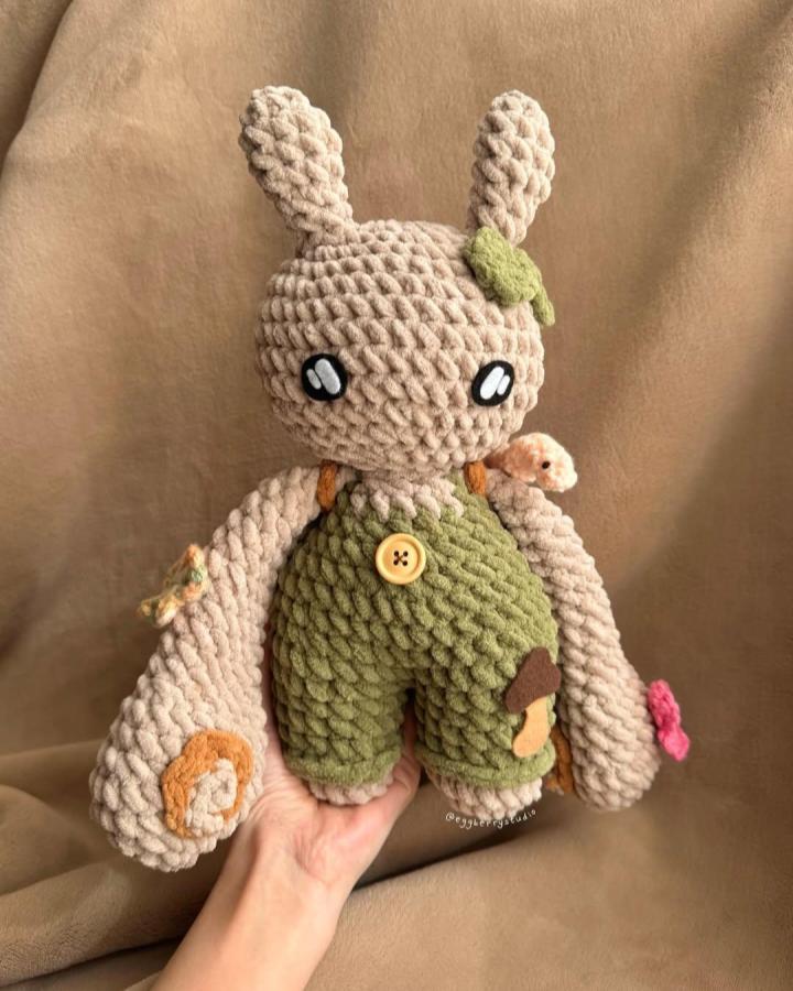 Beige chunky plush bunny with green overalls and forest-themed crochet details from @eggberrystudio. Soft, tactile, and whimsical handmade toy.