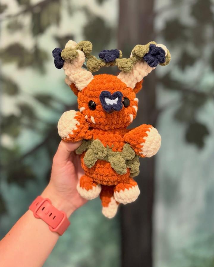 Burnt orange plush crochet creature with leafy green and navy accents from @snapdragoncrocheter. Cozy forest-inspired handcrafted toy.