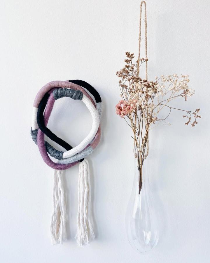 Modern minimalist yarn loop wall hanging with soft grey, mauve, and black yarn by @lilou_studio showing creative yarn wall hanging ideas. Simple yet sculptural.
