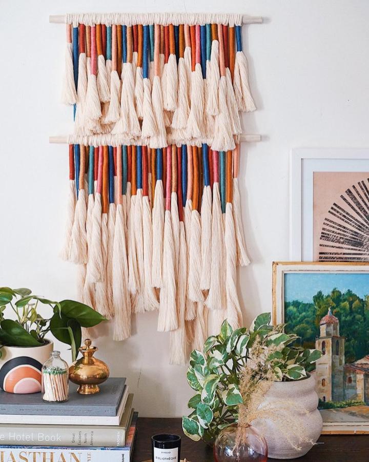 Cream tassel yarn wall hanging with rust and navy accents by @honestlywtf. Cozy boho textured fiber art on wooden dowels.