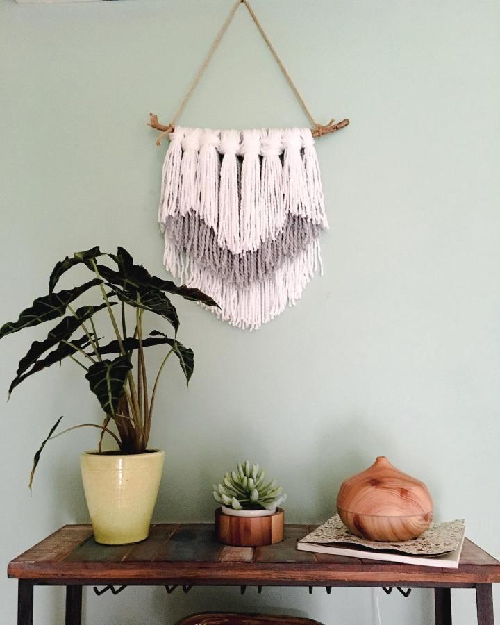 Cream and grey layered yarn wall hanging on rustic wooden branch from @hydrangeasandhappyhour. Soft textured boho decor piece.