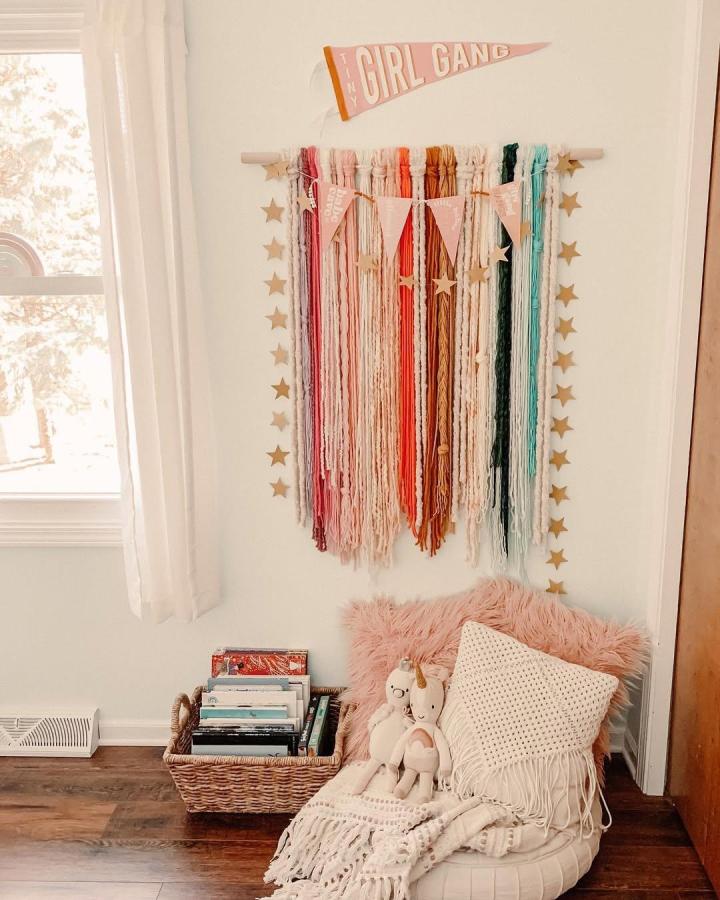 Blush and teal yarn wall hanging with star garland in cozy reading nook by @theheatherco. Cozy and colorful textile art with playful details.
