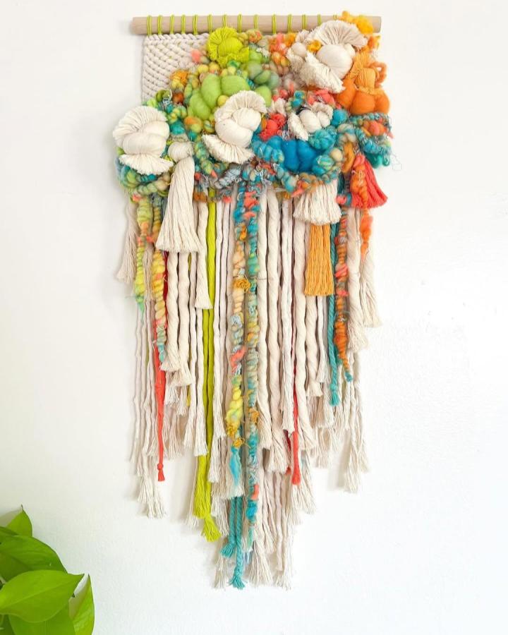 Chunky colorful yarn wall hanging with tassels and pom-poms by @rogueweaving. Bright, textured fiber art for home decor.