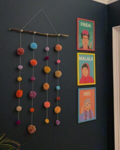 Bright multicolor pom pom mobile hanging on branch from @lulumariaovertherainbow. Cheerful yarn craft with rustic natural wood element.