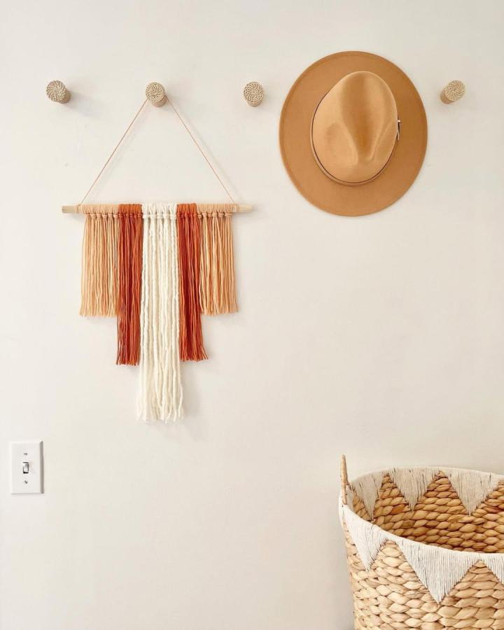 Terracotta and cream yarn wall hanging ideas from @goldenclover_handmade featuring simple vertical strands and natural wood dowel details.