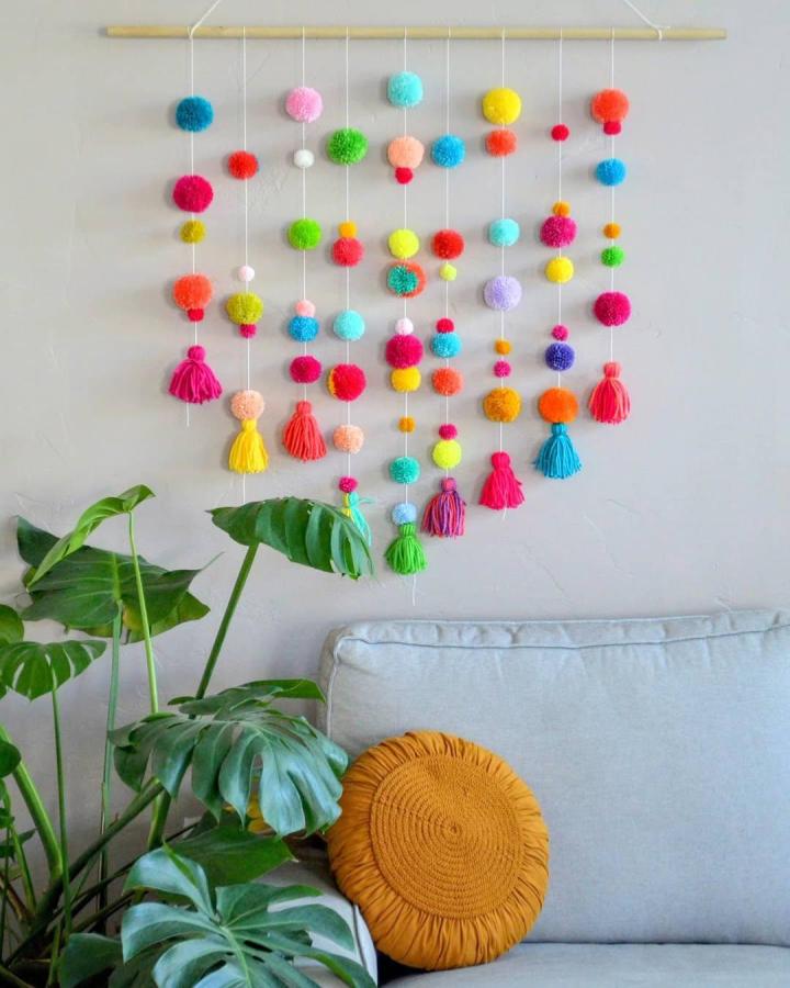 Colorful pom-pom yarn wall hanging with tassels in cozy living room from @apricotpolkadot. Playful and textured fiber art.