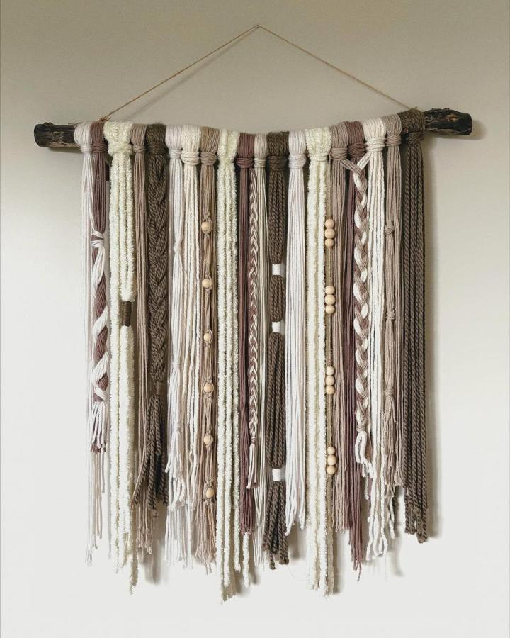 Neutral yarn wall hanging with wooden beads and natural rustic stick from @ivys_daydream soft textured strands in earthy tones.