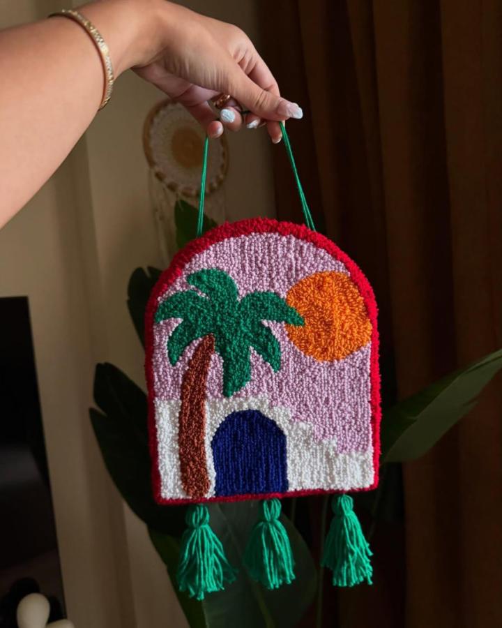Bold colorful punch needle yarn wall hanging ideas with tropical palm tree and tassels from @mernastitches. Bright, textured, playful craft design.