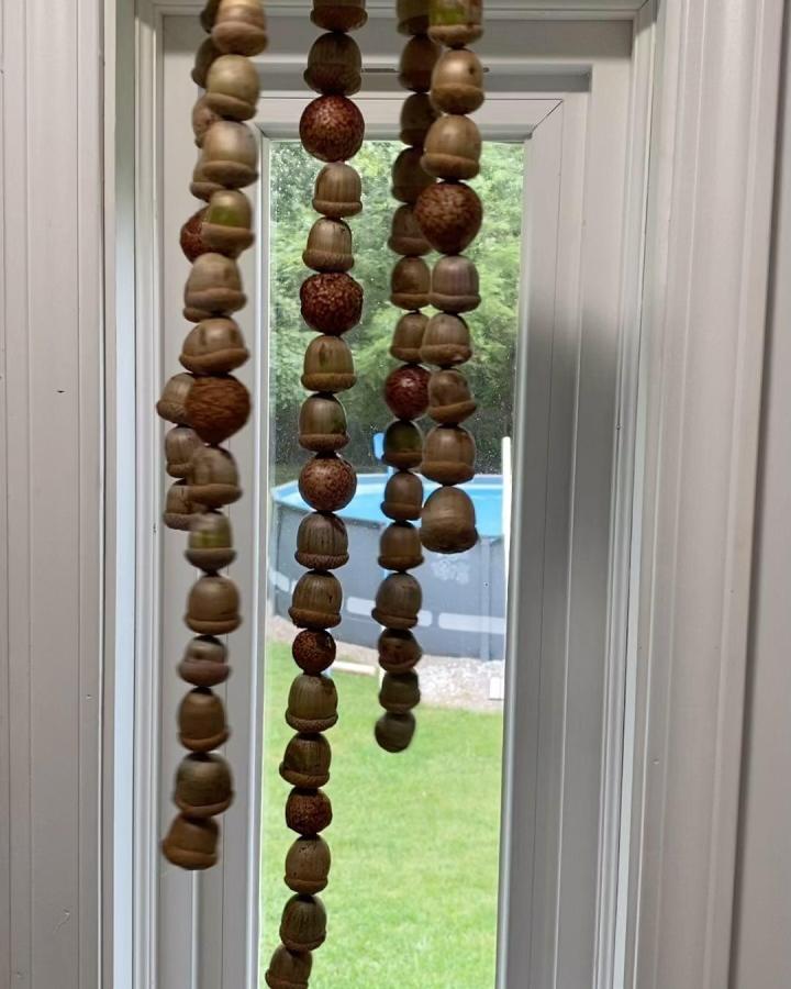 Natural wood and brown acorn chime craft from @tinamsworldoftravel hanging by window for acorn crafts for adults with rustic earthy vibe.