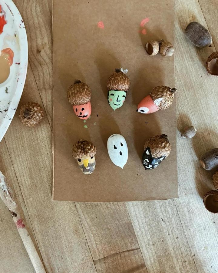 Natural acorn tops with hand-painted faces and whimsical expressions by @_laura_prietto on wooden craft surface. Small playful characters.