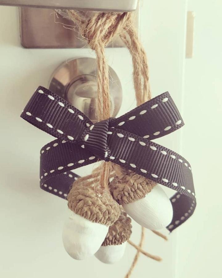 Natural acorn caps with white painted bottoms hanging on rustic twine with black stitched ribbon for door knobs by @rosaechefer simple yet elegant handmade decor.