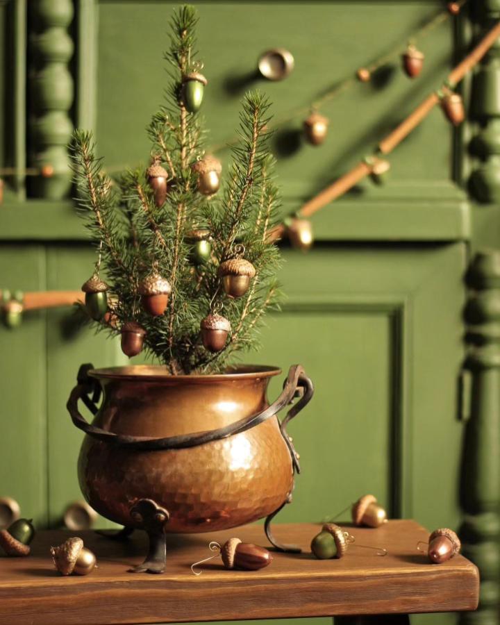 Green and copper miniature Christmas tree with painted acorn ornaments from @lera.perla featuring acorn crafts for adults in a rustic setting.