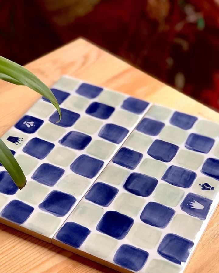 Blue and cream checkerboard handmade tiles with small symbols from @art4funcafe on a wooden surface showing unique brushwork and matte glaze finish.