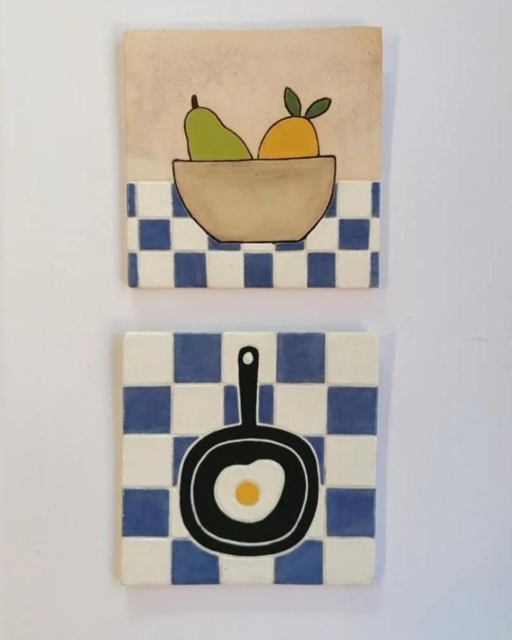 Blue and white checkerboard ceramic tile crafts wall art from @kendalwarren featuring kitchen motifs like fruit bowl and frying pan. Classic and cozy design.