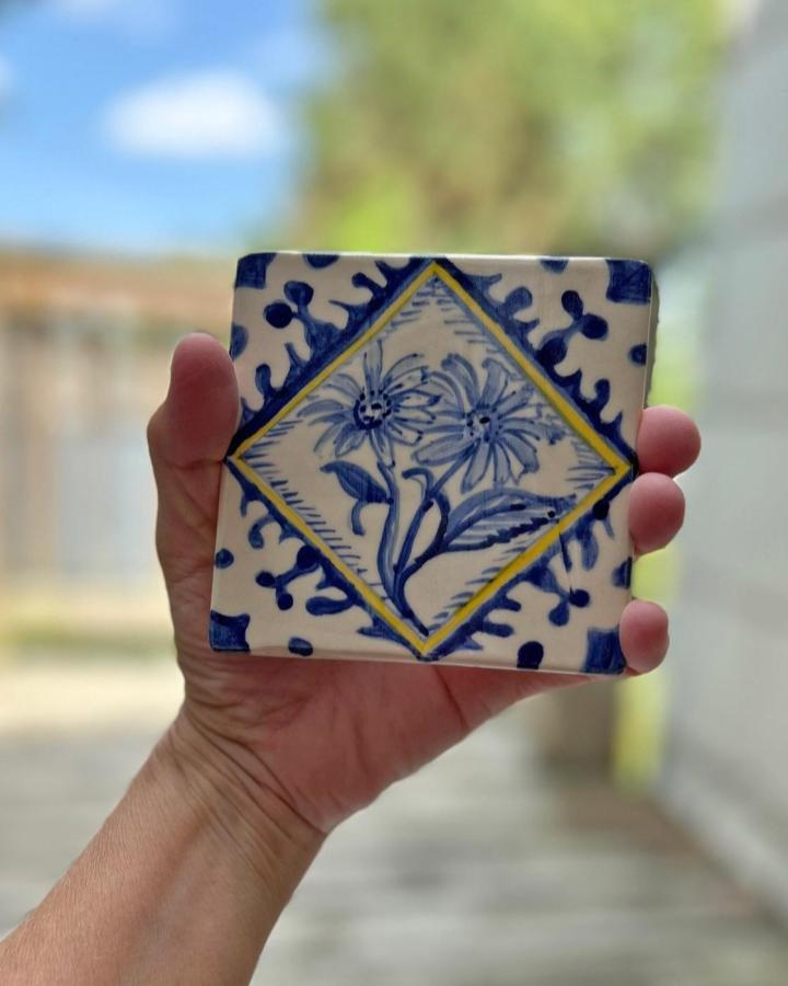 Blue and yellow handpainted floral tile held in hand from @pattysheppardart. Classic hand-drawn brushstroke design.