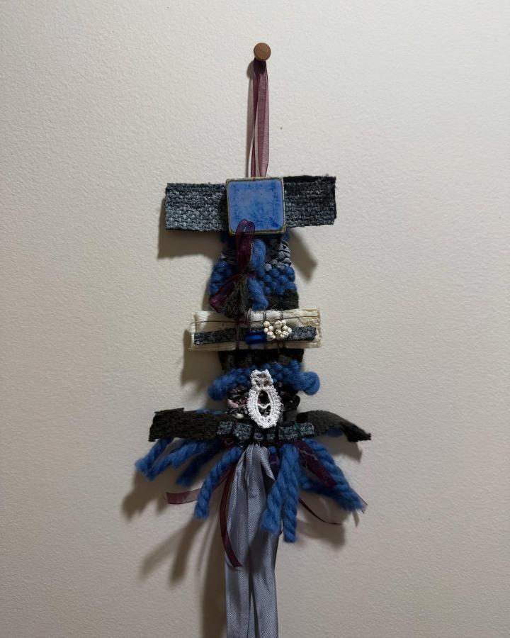 Blue ceramic tile wall hanging with yarn and ribbon details by @kocomagik2.0. Mixed materials create rich texture and bold contrast.