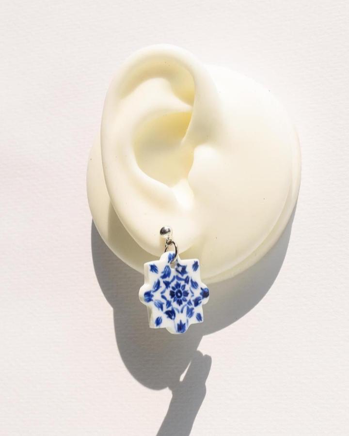 Blue and white floral porcelain earring inspired by tile designs from @inthaistudio displayed on a white ear model.