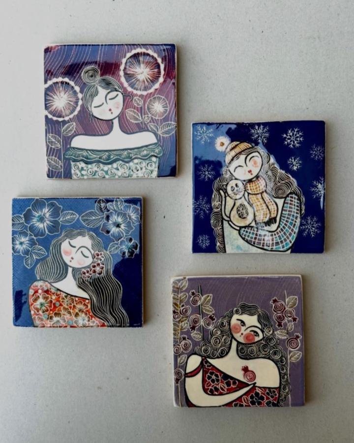 Four square ceramic tiles decorated with whimsical female portraits featuring floral and winter motifs by @silk.copper. Hand-painted delicate and colorful artisan tile decor.