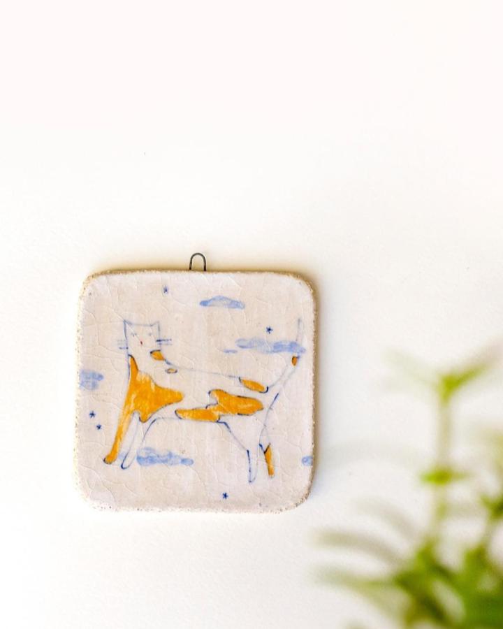 Orange and blue illustrated cat ceramic tile wall decor from @partofpolly featuring whimsical ceramic tile crafts in a soft cream background.