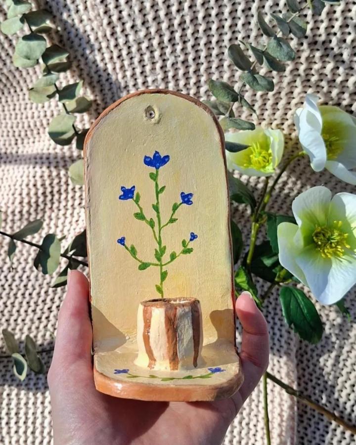 Terracotta and handpainted floral clay candle holder from @beaudine.arts with soft yellow background and blue flowers.
