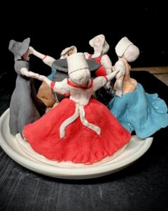 Clay dancing women candle centerpiece by @emily_gravett. Colorful hand-sculpted figures holding hands around a central candle plate.