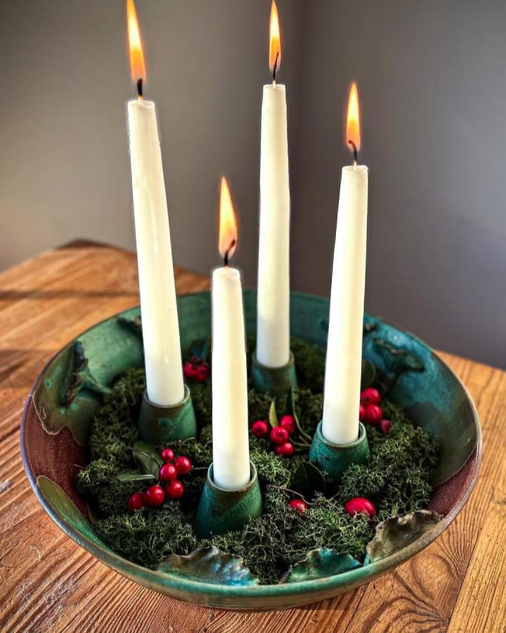 Rustic green glazed clay candle holder craft ideas from @sabina.morin.studio with moss and red berry accents on wooden table.
