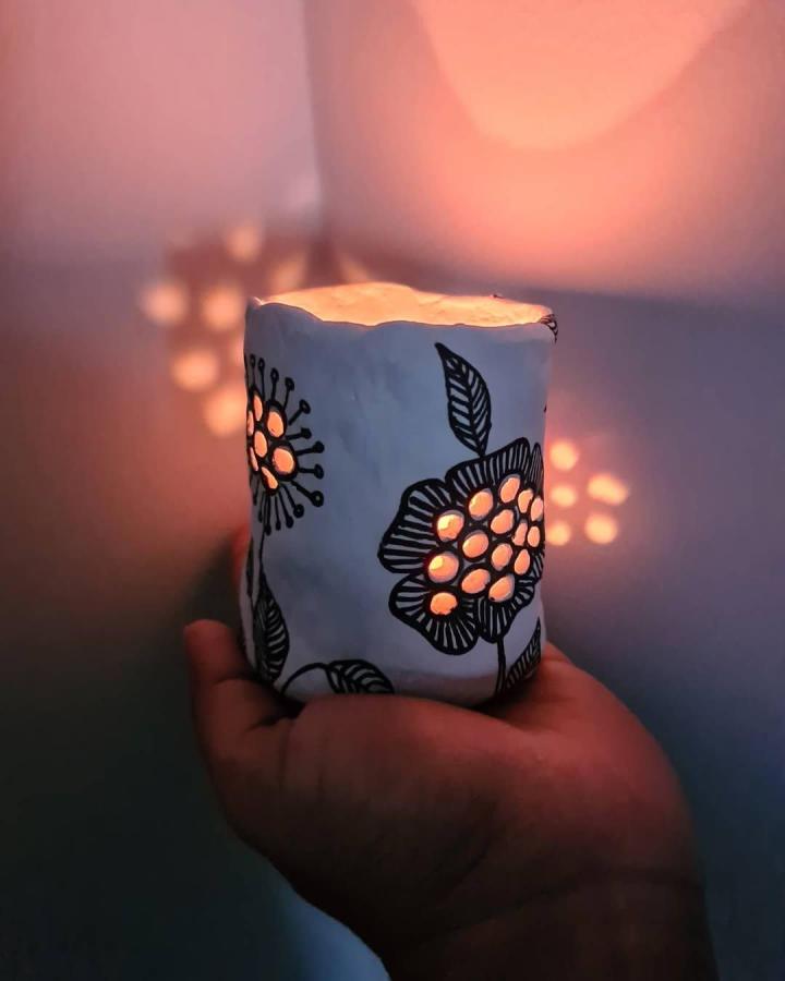 White clay candle holder with black hand-painted flowers and glowing perforations by @girl.in.d.city creating cozy lighting effects.