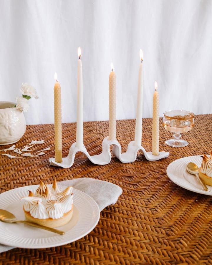White wave-shaped ceramic candle holder on woven table with mixed beeswax and white candles by @jaharnquinn for stylish home decor.